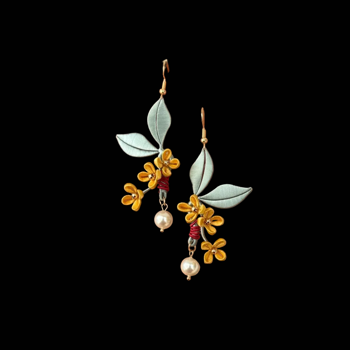 Close-up of Chanhua osmanthus earring showing thread-wrapped yellow flowers and sage green leaf detail with red wire wrap