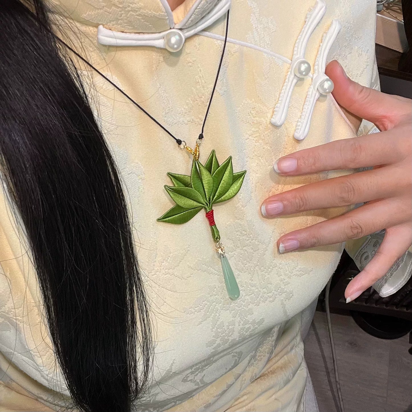 A handmade Chanhua pomelo - leaf necklace with a green leaf pendant, red - wrapped base, and light green teardrop charm worn on a yellow traditional garment-2