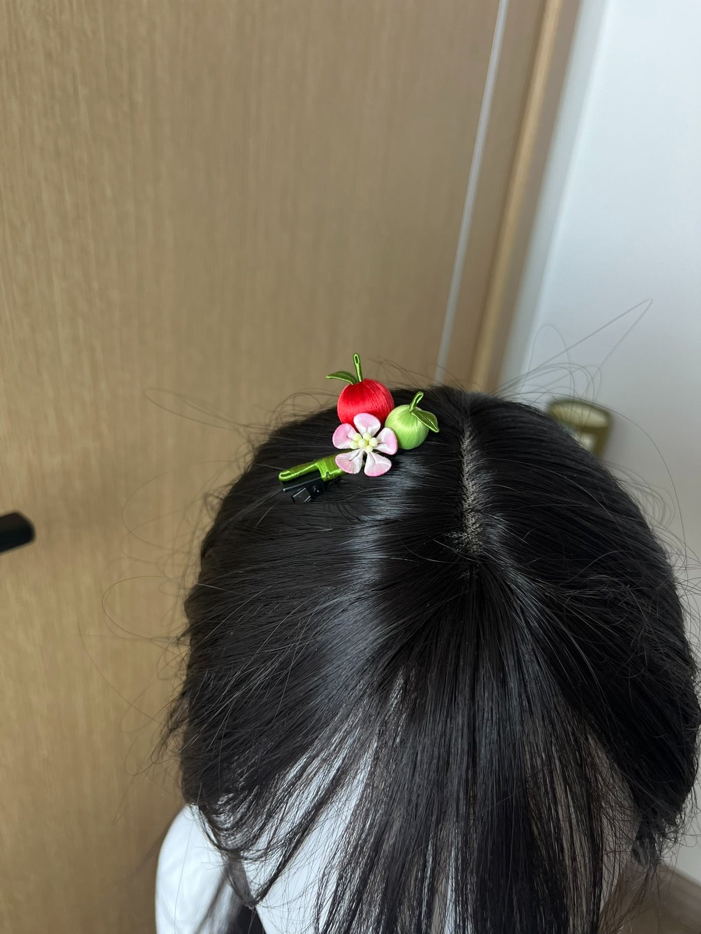 A hair clip with red and green apples and a pink flower on black hair