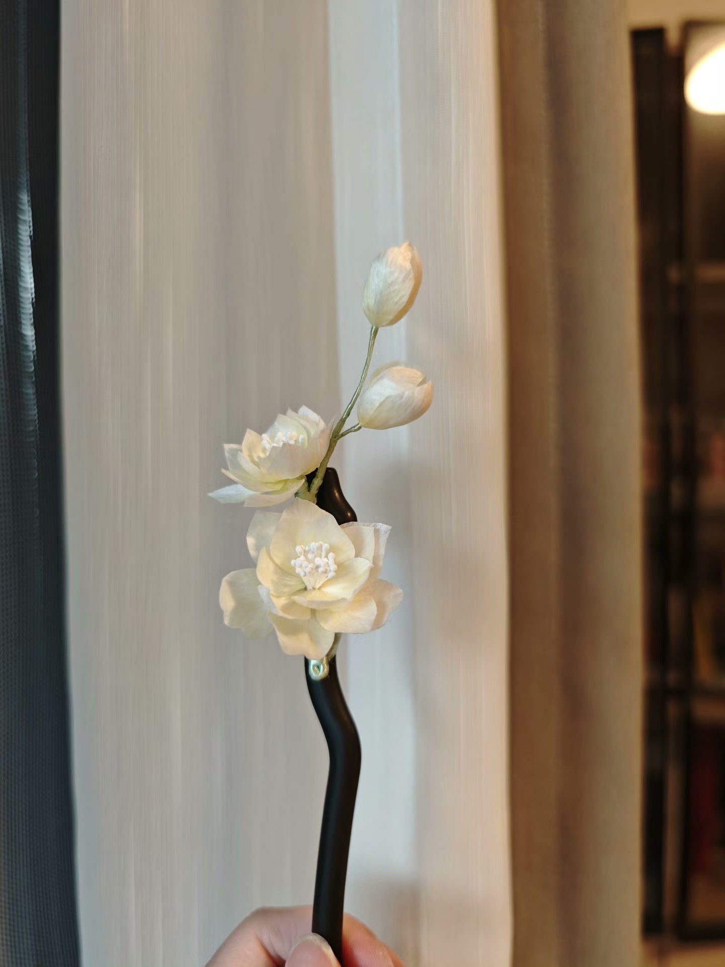 Handmade Ronghua white jasmine hairpin with lifelike flowers held against a light - colored background