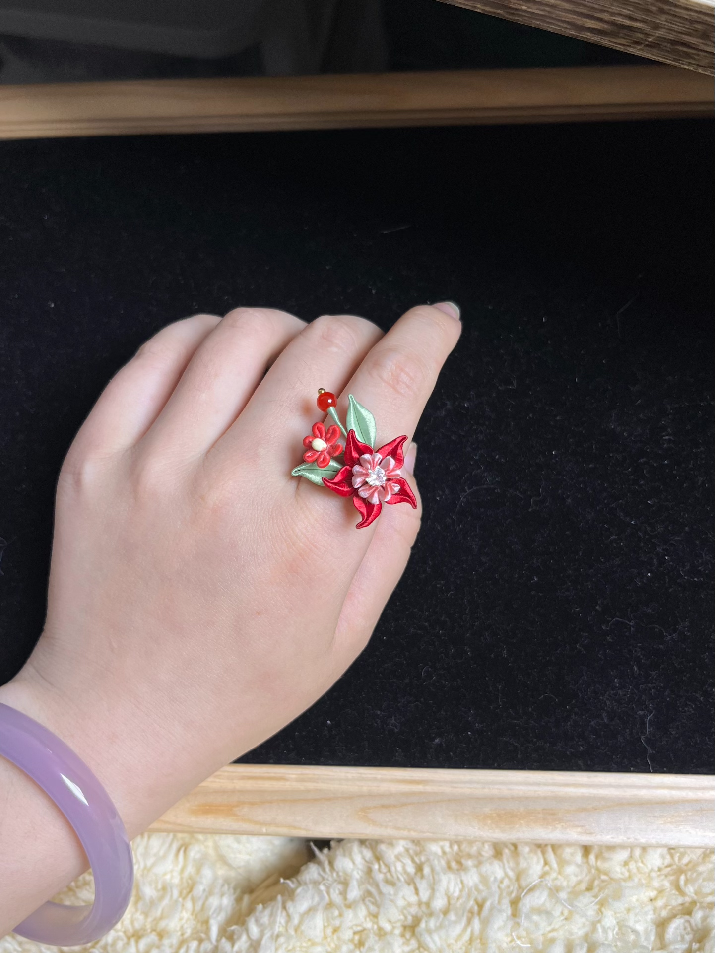 A hand wearing a vibrant red Handmade Chanhua Mandala Ring with green leaves and pink details-2