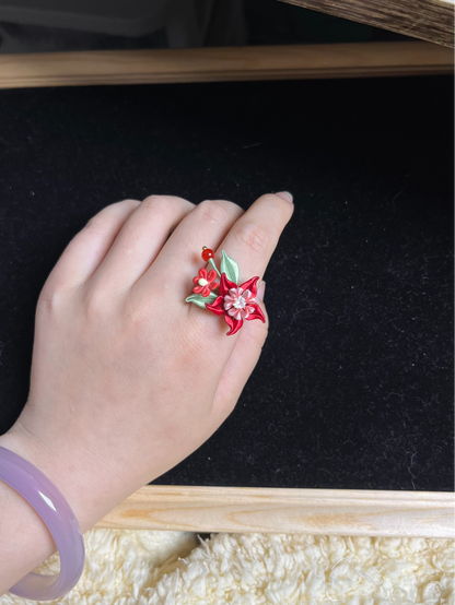 A hand wearing a vibrant red Handmade Chanhua Mandala Ring with green leaves and pink details-2