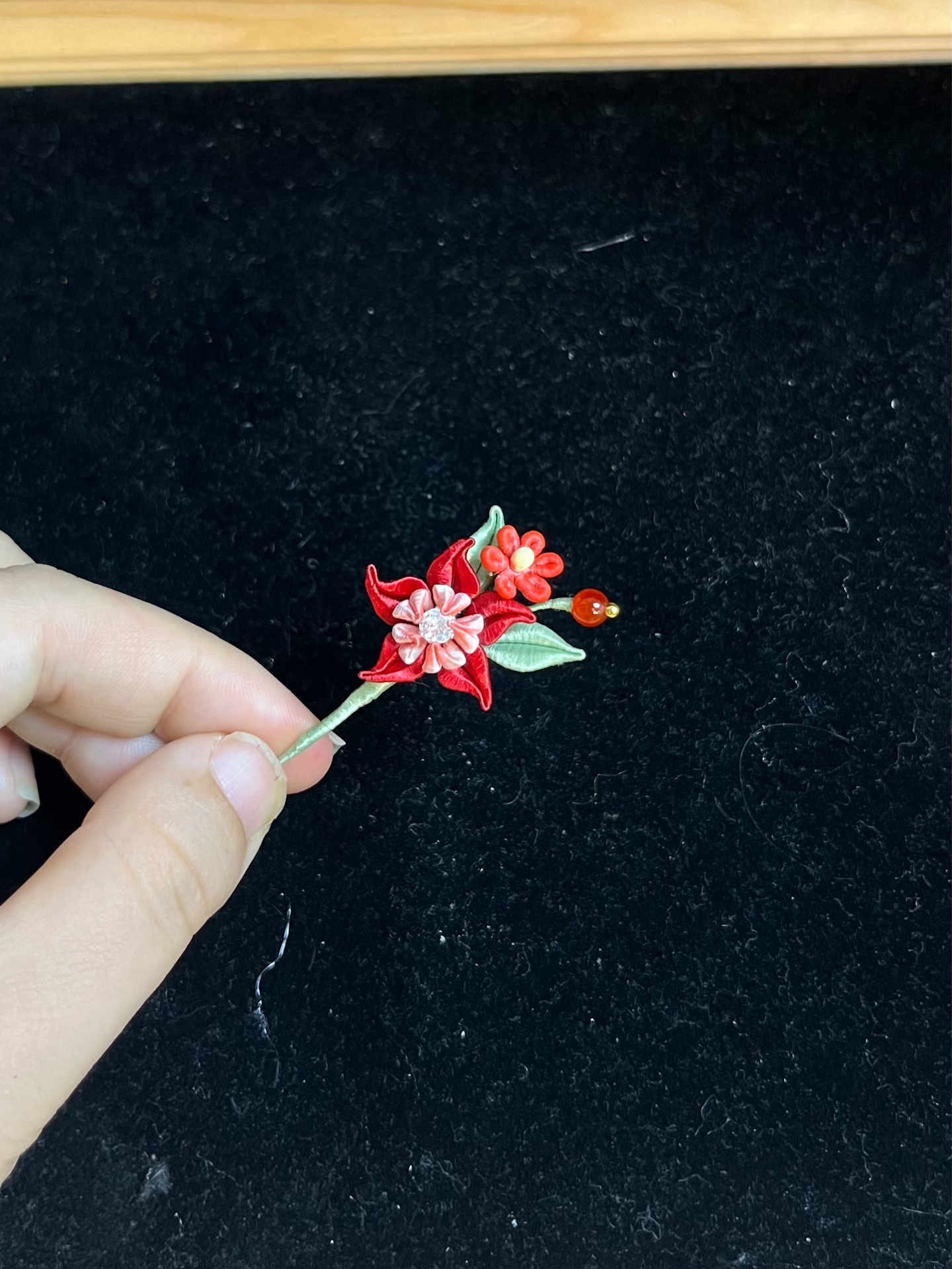 A hand wearing a vibrant red Handmade Chanhua Mandala Ring with green leaves and pink details-4