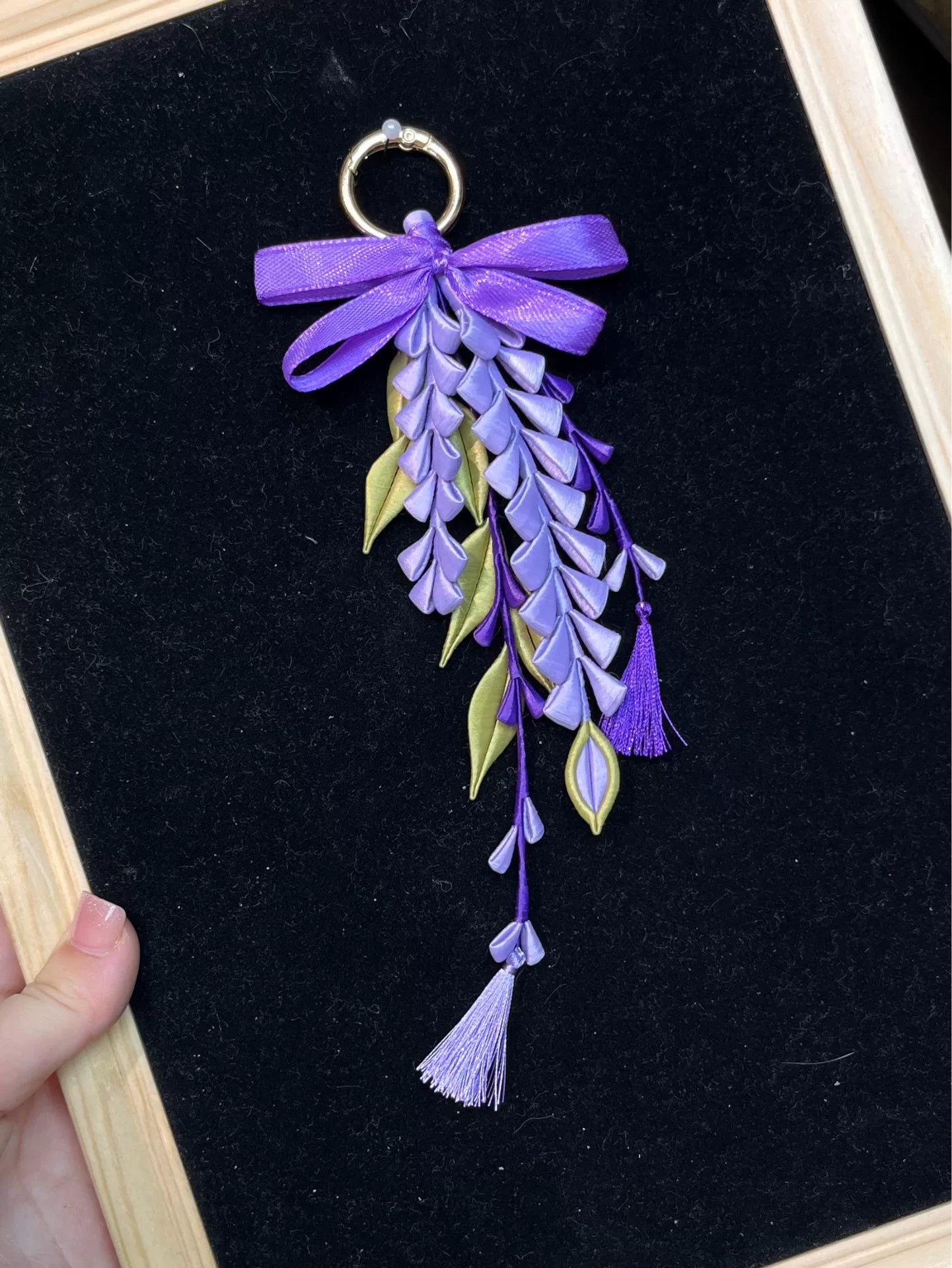 A hand - held purple wisteria keychain with a golden ring and decorative bow-5