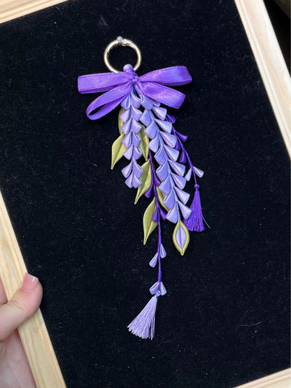A hand - held purple wisteria keychain with a golden ring and decorative bow-5