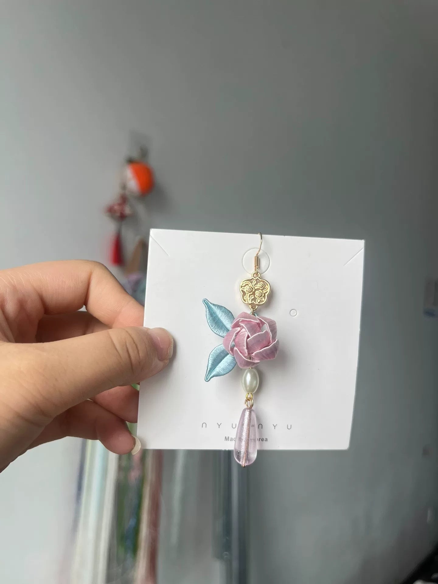 Handmade Chanhua earrings with a pink flower, blue leaves, a golden charm, and a pearl