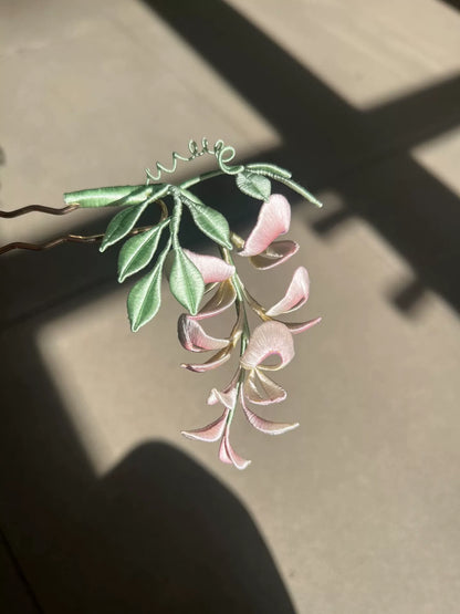 A handmade Chanhua wisteria flower accessory with pink petals and green leaves