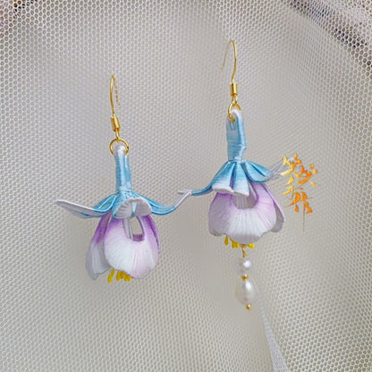 A pair of delicate, handcrafted Chanhua flower earrings with light blue and purple petals, showcasing the intricate details of the fabric and the 925 sterling silver ear hooks against a sheer white background.