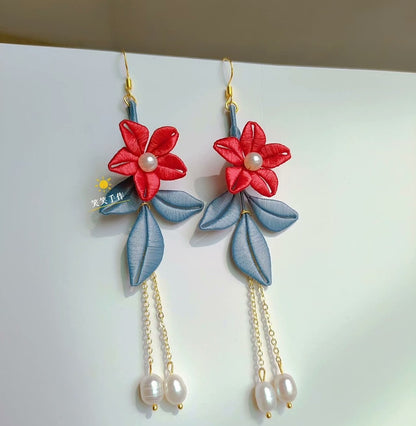 A pair of handcrafted red Chanhua floral earrings with blue-grey leaves and dangling white freshwater pearls, displayed against a white background.