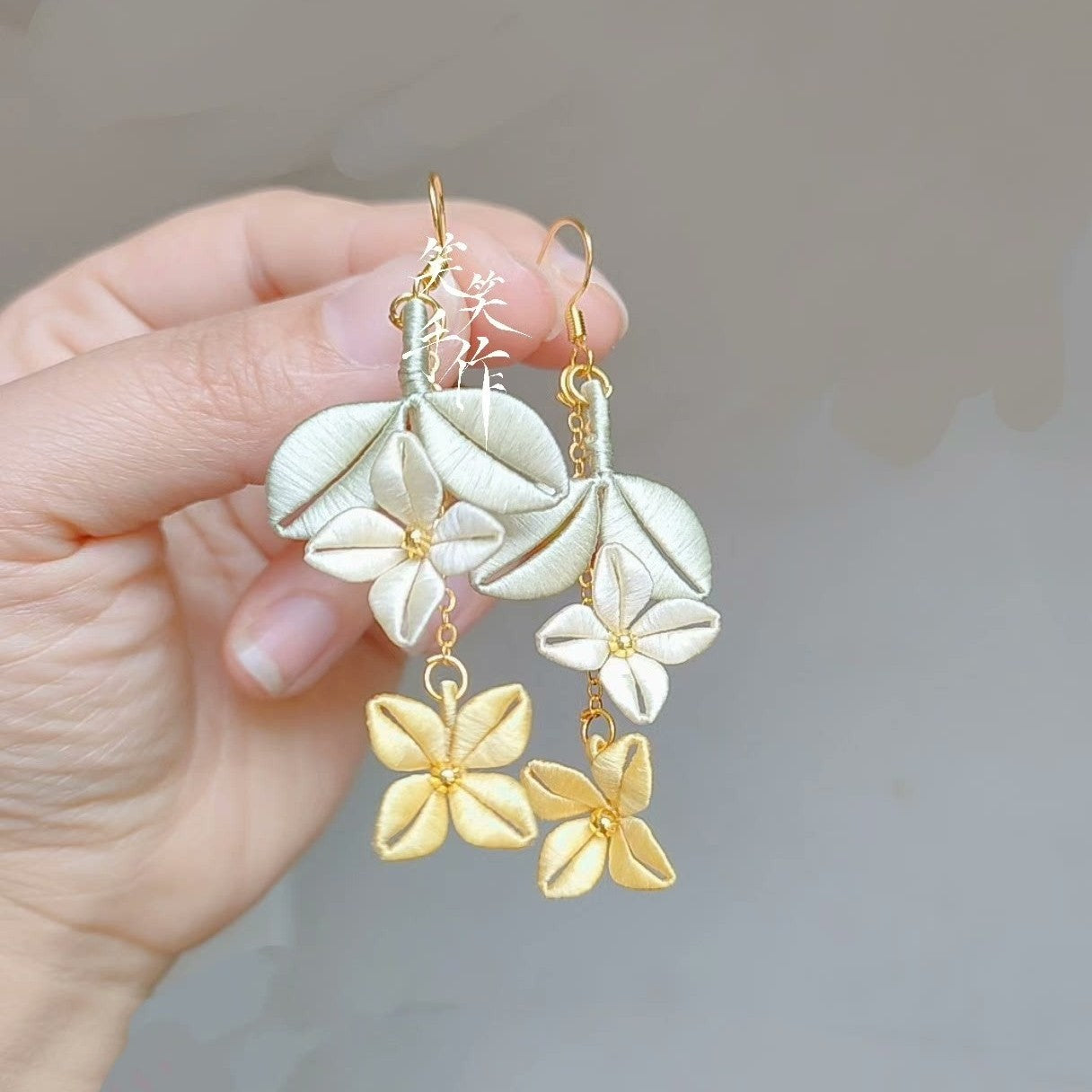Chanhua silk embroidered earrings, handmade with delicate green and cream petals and golden floral accents, on a white background, showcasing intricate detail and elegant design.