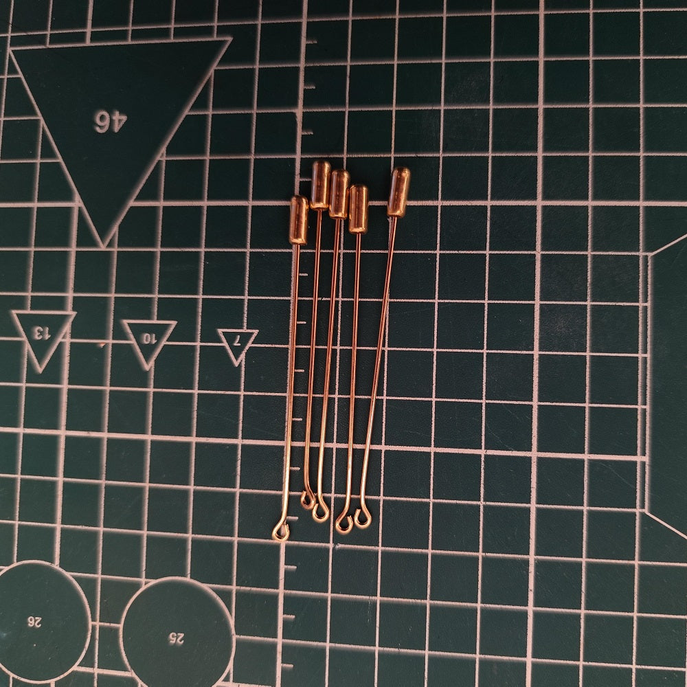 Five gold-tone alloy lapel pin bases with loop ends, arranged on a green cutting mat.