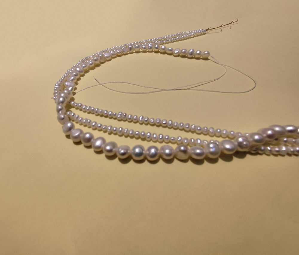Assorted sizes of natural baroque pearls on string, showcasing their unique forms.